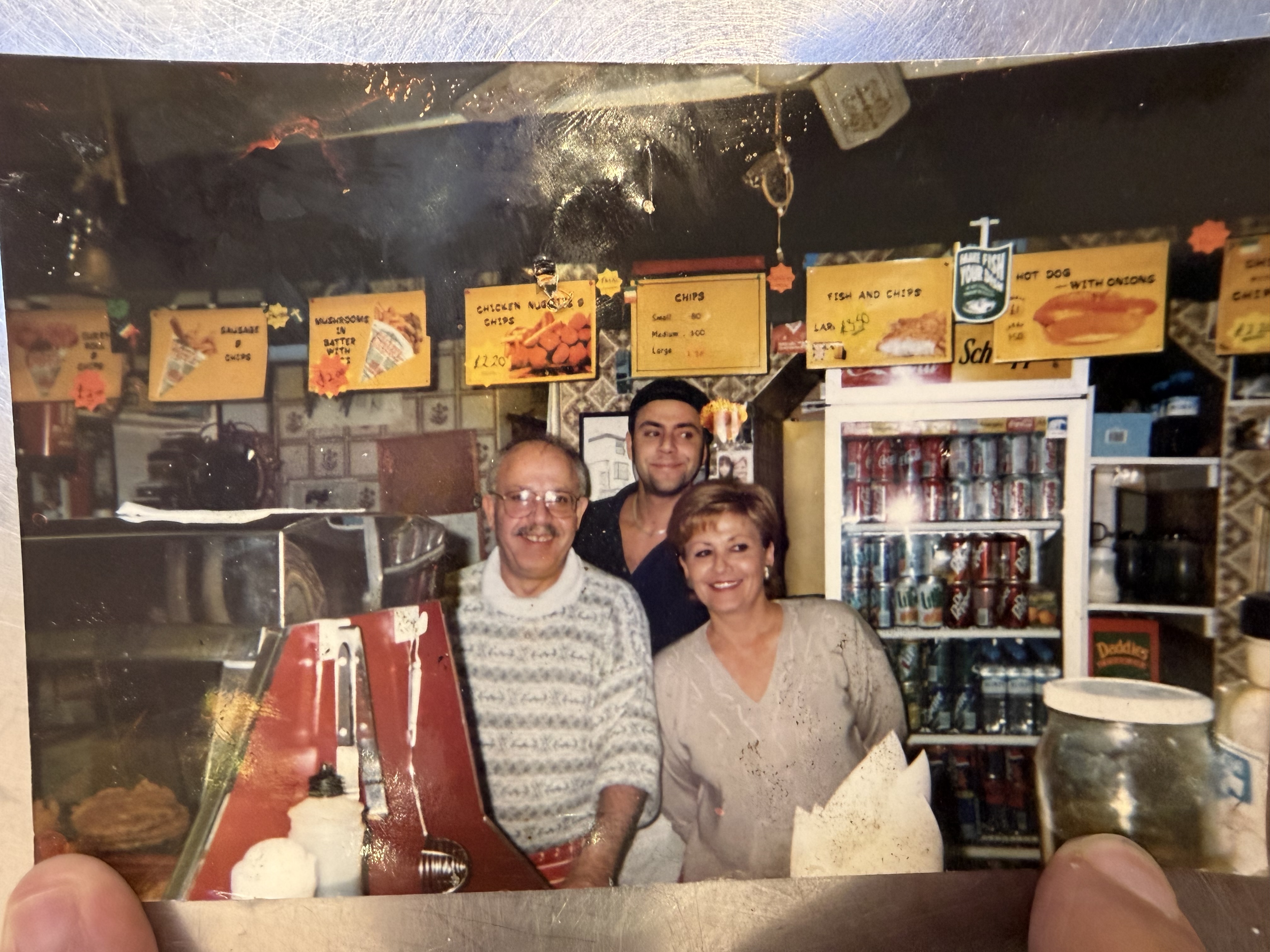 Three people smiling behind the City Fish Bar counter in a photograph from the family album